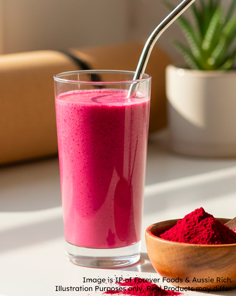 Pink beetroot smoothie in a glass with a straw, next to a wooden bowl of red powder on a light surface.