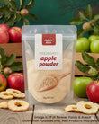A stand-up pouch of Aussie Rich Freeze Dried Apple Powder, surrounded by fresh red and green apples, dried apple slices, and a dark green background with leafy branches.