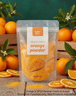 A stand-up pouch of Aussie Rich Freeze Dried Orange Powder centered on a rustic wooden surface, surrounded by whole oranges, sliced oranges, and green leaves against a dark green background.