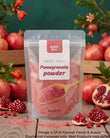 A 50g stand-up pouch of Aussie Rich Freeze Dried Pomegranate Powder, displayed on a rustic wooden surface surrounded by fresh pomegranates and green leaves against a dark green background.
