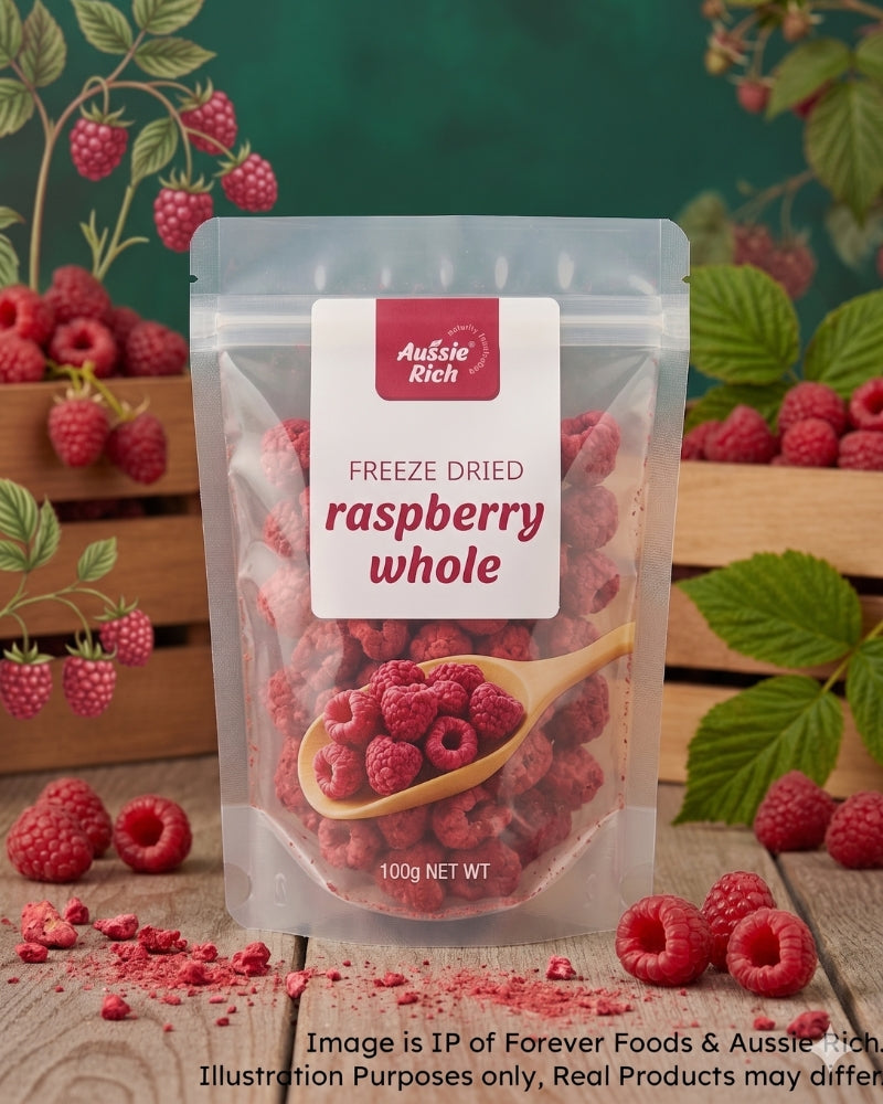 A stand-up pouch of Aussie Rich Freeze Dried Raspberry Whole, shown on a rustic wooden surface with fresh raspberries, leaves, and crates in the background. The pouch is clear enough to show the freeze-dried raspberries inside, with a white label featuring red text and a wooden spoon graphic.