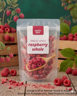 A stand-up pouch of Aussie Rich Freeze Dried Raspberry Whole, shown on a rustic wooden surface with fresh raspberries, leaves, and crates in the background. The pouch is clear enough to show the freeze-dried raspberries inside, with a white label featuring red text and a wooden spoon graphic.