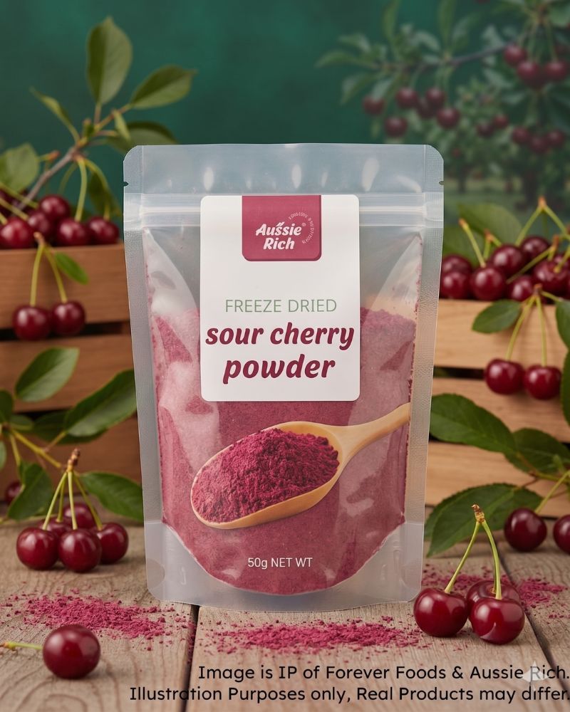 A stand-up pouch of Aussie Rich Freeze Dried Sour Cherry Powder, displayed on a rustic wooden surface surrounded by fresh cherries and green leaves against a dark green background.
