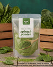 A stand-up pouch of Aussie Rich Freeze Dried Spinach Powder, displayed on a rustic wooden surface with fresh spinach leaves and a wooden crate in the background.
