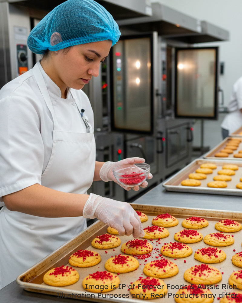 Person in a kitchen preparing food with a tray of cookies and sprinkling Freeze Dried Raspberry Crumbs.