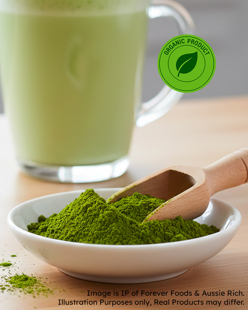 Green moringa powder in a bowl with a wooden scoop, next to a glass of green liquid, on a wooden surface.
